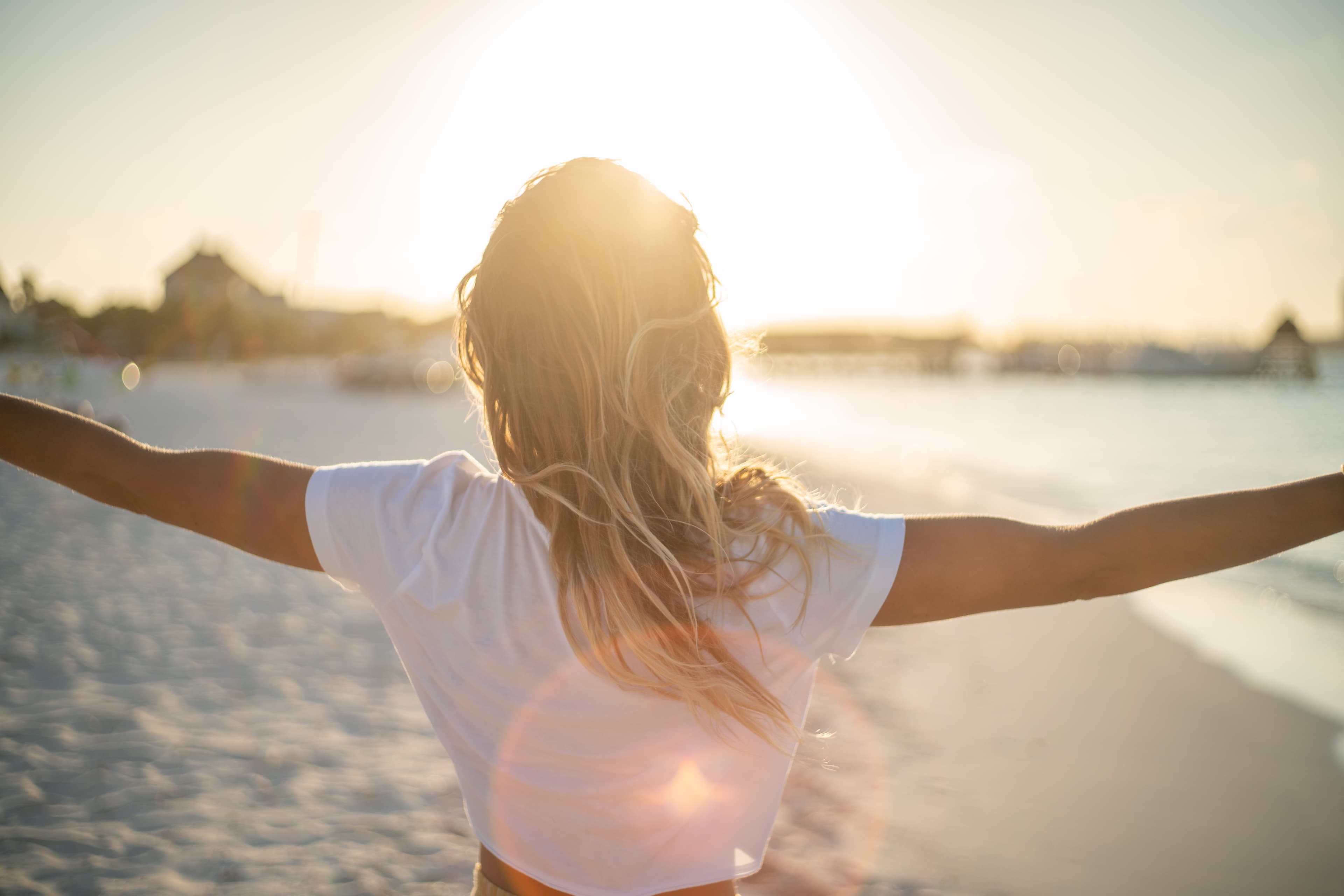 A woman facing away with her arms outstretched and the sun in front of her